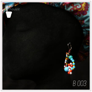 Boucles d'oreilles montées sur dormeuses en acier.Perles multicolores en verre et rocailles multicolores. Dominante bleue turquoise et rouge Vu de profil sur une tête de mannequin