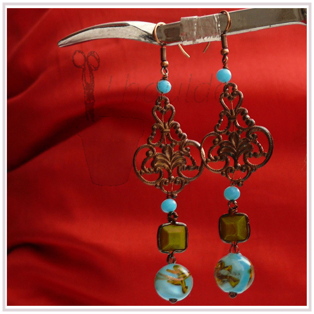 Boucles d'oreilles longues montées sur crochet d'acier, petite perle ronde couleur turquoise, estampe couleur bronze, petite perle ronde couleur turquoise, perle carrée vert-jaune enchassée dans de l'acier, perle bleue ronde à incrustation dorée