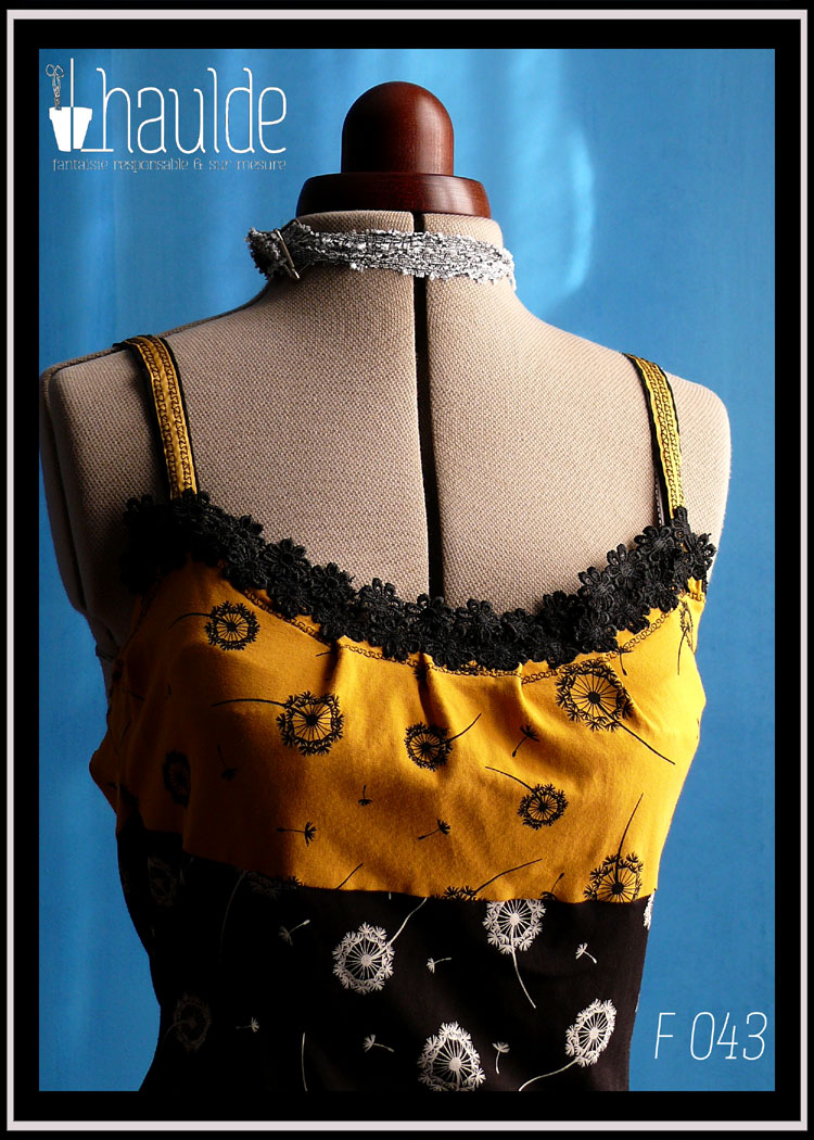 robe mi-longue à bretelles, en jersey jaune imprimé aigrettes de pissenlits noirs jusqu'en dessous du buste et jersey noir imprimé aigrettes de pissenlits blancs pour le bas. Les bretelles sont jaunes piquées de motifs noirs et une dentelle de fleurs noires court en haut de la robe Vue de détail du buste