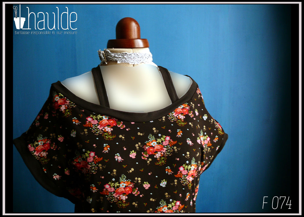 Robe sans manche col bateau, haut en jersey noir imprimé fleurs rouges et roses avec des points dorés, bas en jersey noir. Deux bretelles maintiennent les épaules en place Vue de détail du haut