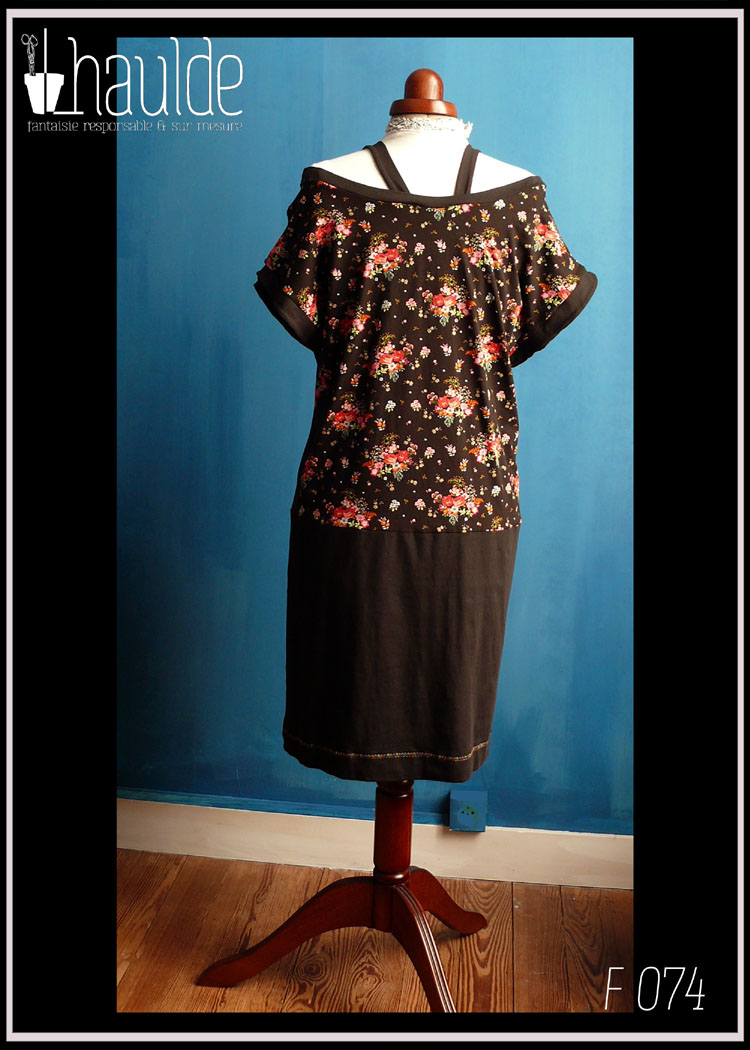 Robe sans manche col bateau, haut en jersey noir imprimé fleurs rouges et roses avec des points dorés, bas en jersey noir. Deux bretelles maintiennent les épaules en place Vue de dos en pied sur un mannequin couture