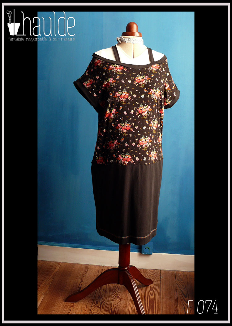 Robe sans manche col bateau, haut en jersey noir imprimé fleurs rouges et roses avec des points dorés, bas en jersey noir. Deux bretelles maintiennent les épaules en place Vue de face en pied sur un mannequin couture