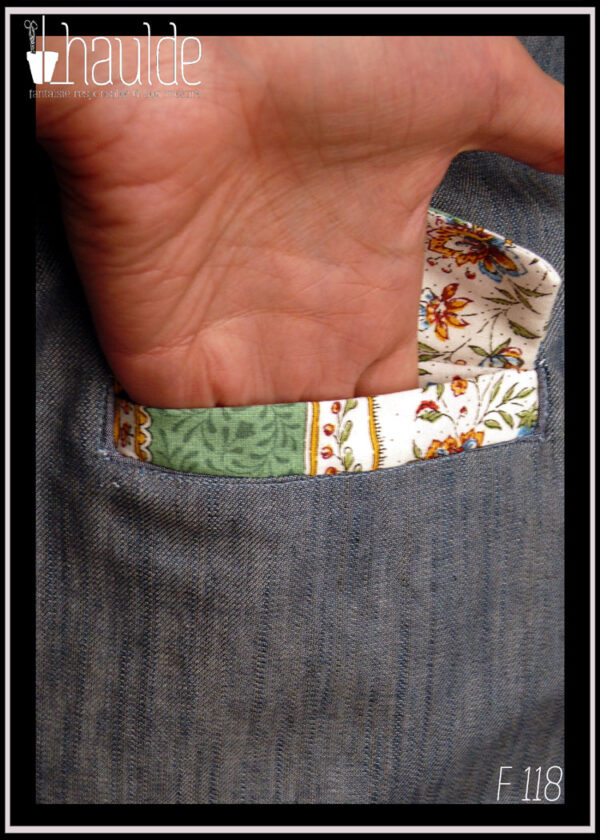 Veste tailleur évasée en jean et tissu provençal, deux poches sur l'avant. Manches, col, rabats des poches et doublure en tissu provençal fond blanc colonnes vert pâle, le reste en jean bleu Vue de détail d'une poche avec une main qui se glisse dedans