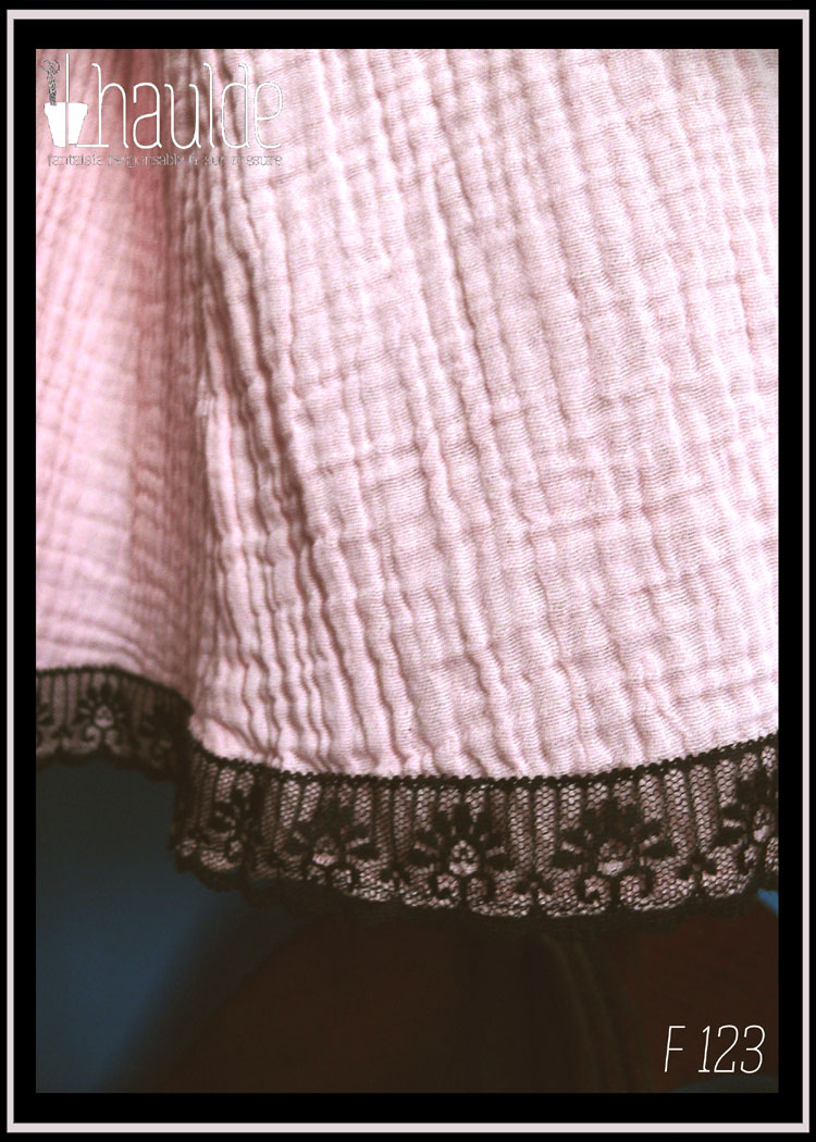 plan rapproché du bas de la jupe Robe d'été à bretelles en double gaze rose pâle, galon de dentelle noire au bas de la robe, biais noir autour du haut du buste. buste plissé, taille ajustée, jupe évasée.