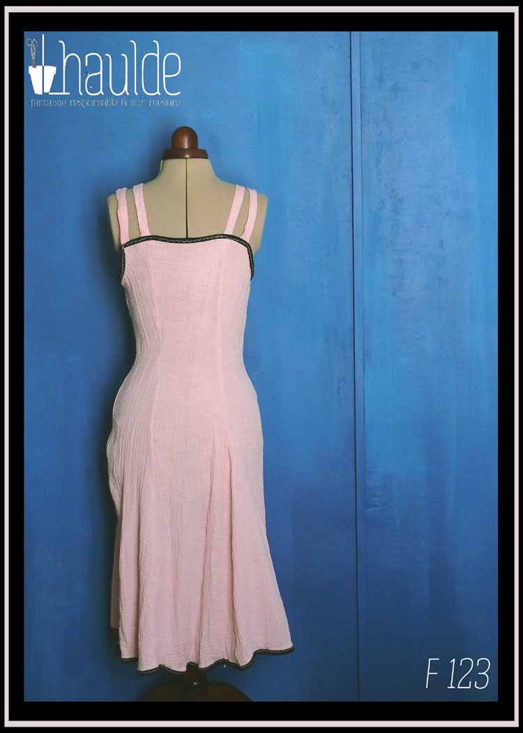 Robe d'été à bretelles en double gaze rose pâle, galon de dentelle noire au bas de la robe, biais noir autour du haut du buste. buste plissé, taille ajustée, jupe évasée. Vue de dos sur un mannequin de couture