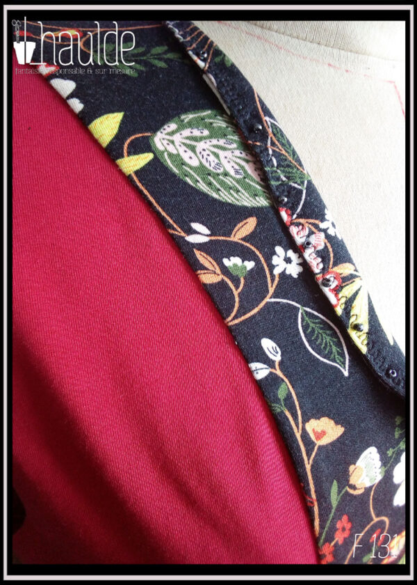 Robe mi-longue, manches mi-longues évasées en jersey, noir imprimé fleurs au centre sur toute la longueur devant et pour les manches. Jersey rouge cerise pour les côtés et le dos. Vue de détail du col