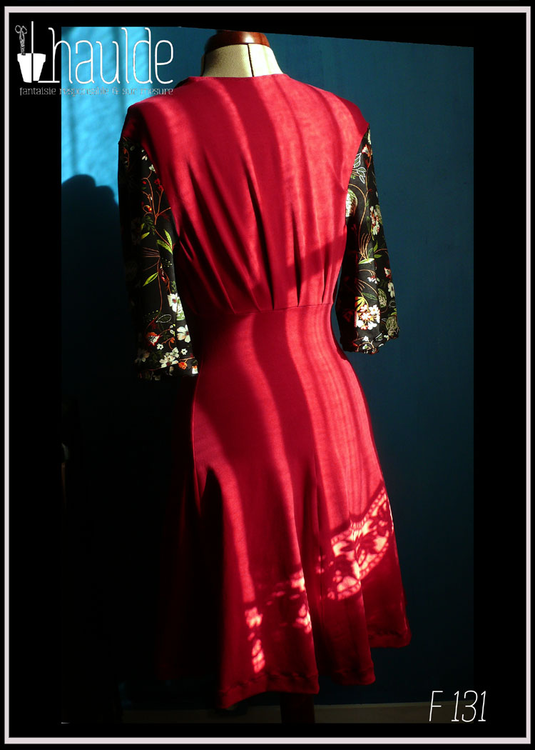 Robe mi-longue, manches mi-longues évasées en jersey, noir imprimé fleurs au centre sur toute la longueur devant et pour les manches. Jersey rouge cerise pour les côtés et le dos. vue de dos en pied sur un mannequin couture