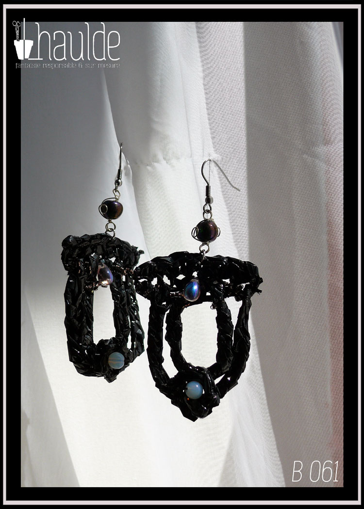 Boucles d'oreilles longues en bande VHS crochetée et garnies de perles bleu pâles iridescentes. Leur forme est un double U fermé en haut. Vue de face au soleil sur fond blanc