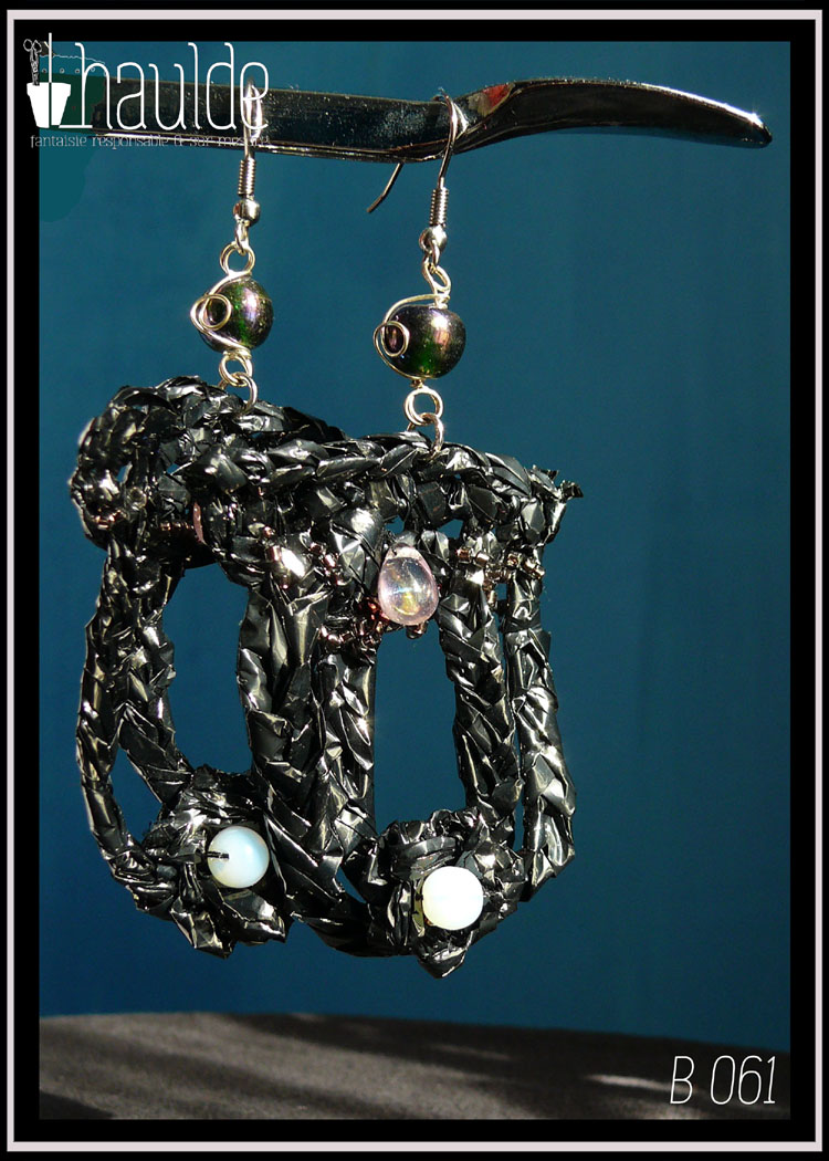 Boucles d'oreilles longues en bande VHS crochetée et garnies de perles bleu pâles iridescentes. Leur forme est un double U fermé en haut. Vue de détail au soleil sur fond sombre