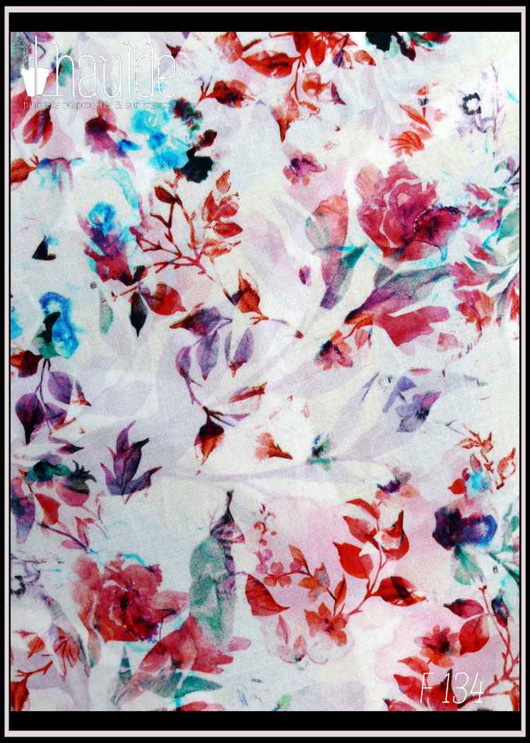 vue de détail du tissu, fond blanc imprimé motifs floraux et végétaux façon aquarelle, dominante rouge avec des touches de bleu vif, mauve et vert discret