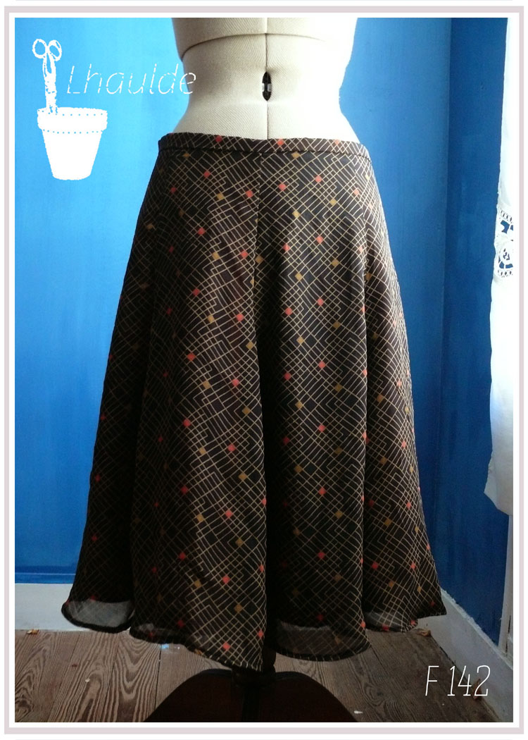 jupe mi longue à pans amples en toile de coton et lin recouverte de voile noir imprimé de lignes perpendiculaires formant de temps en temps des carré à leur intersection (rouge, doré et noir)