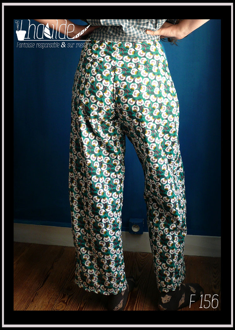 Pantalon en tissu imprimé motifs abstraits qui évoquent des fleurs très stylisées blanches sur fond émeraude Vu porté de dos