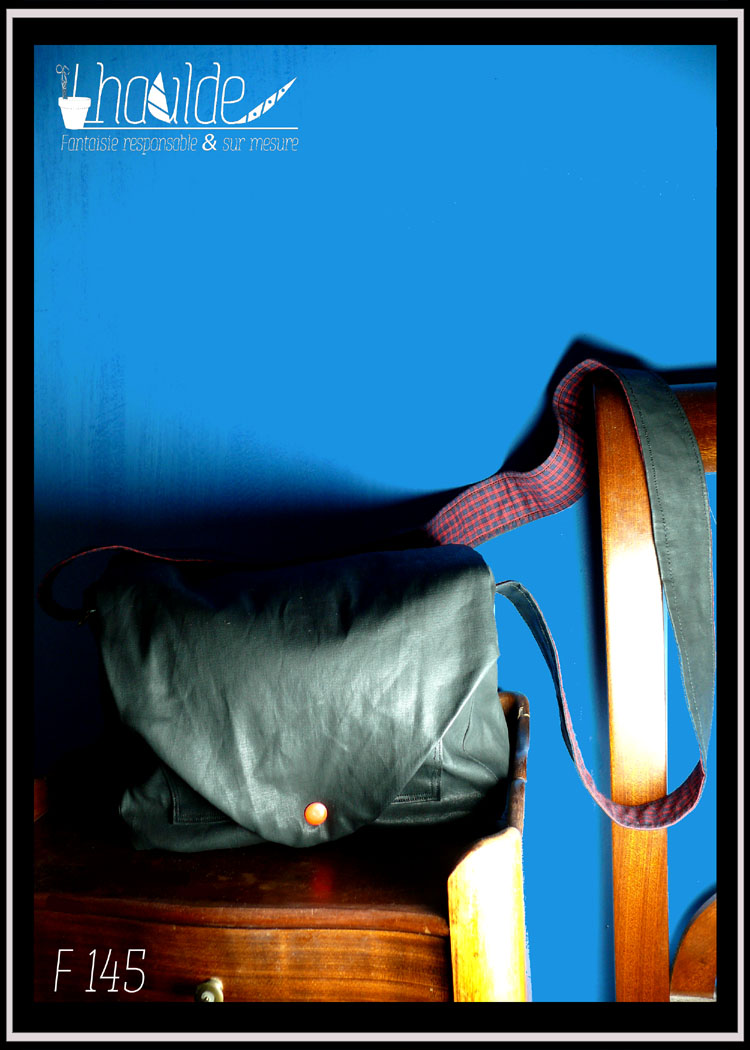 petit sac en simili cuir noir vu fermé d'un rabat à bouton pression rouge et posé sur un meuble