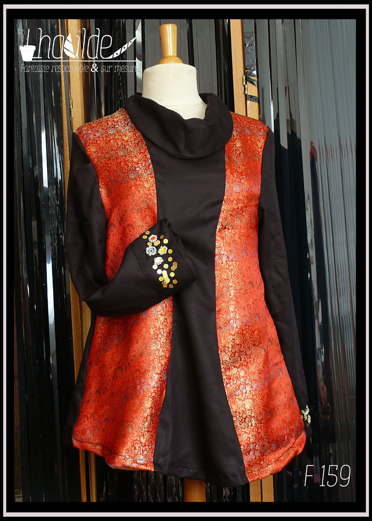 Tunique longue à manche longue. Centre, col, manches et dos en tencel noir. Manchettes brodées de perles et de miroirs. Côtés devant en soie rouge brocardée de motifs dorés Vue de face sur un mannequin de couture