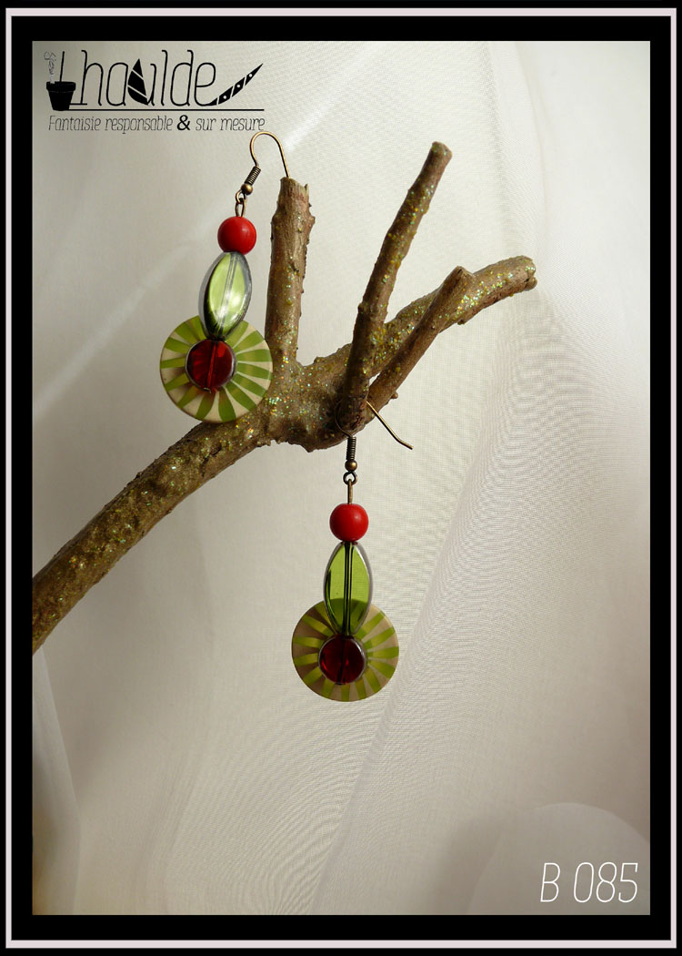 Paire de boucles d'oreilles, crochet acier. Bouton vintage en plastique rayé vert et vert pâle (les rayures partent du centre du bouton vers l'extérieur, comme des rayons) monté sur tige acier avec en son centre une perle en verre rouge avec une tranche en acier, au dos une perle en verre rouge biseauté et au-dessus une perle oblongue en forme de feuille en verre vert avec tranche acier et une perle en verre opaque rouge. Longueur 6,5 cm