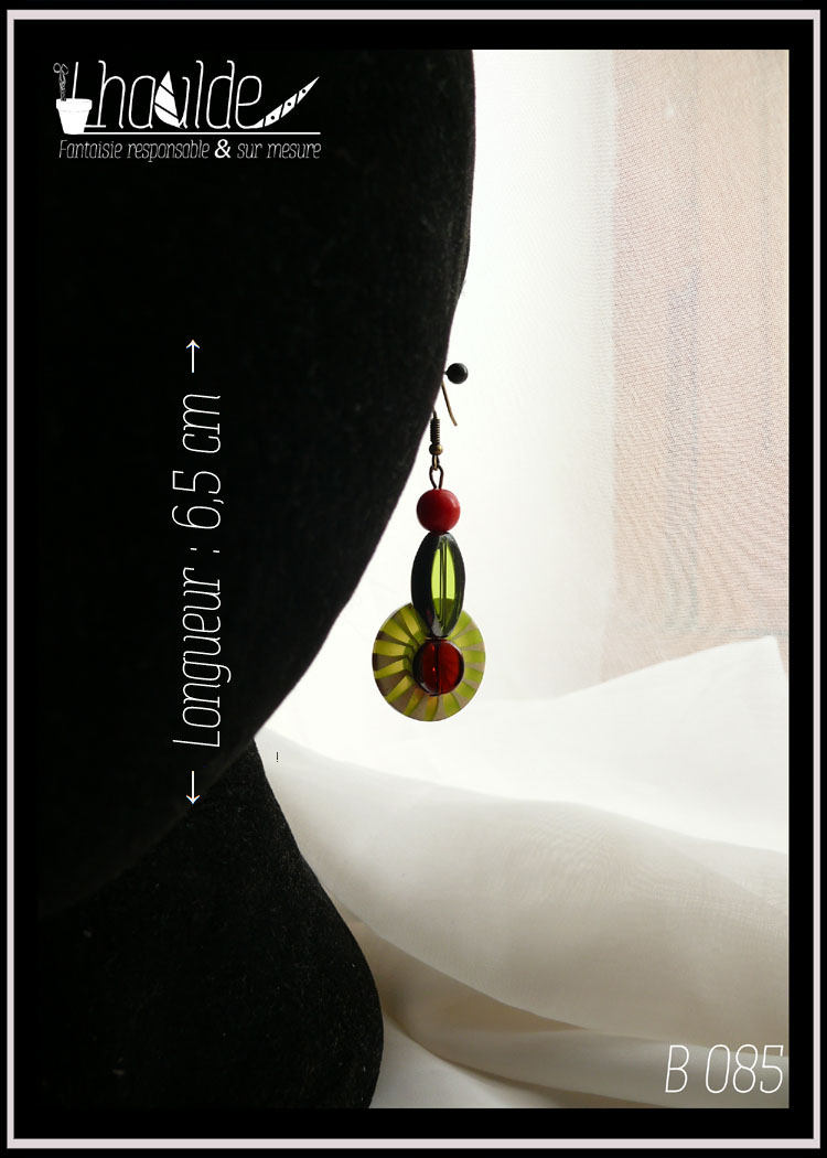 Paire de boucles d'oreilles, crochet acier. Bouton vintage en plastique rayé vert et vert pâle (les rayures partent du centre du bouton vers l'extérieur, comme des rayons) monté sur tige acier avec en son centre une perle en verre rouge avec une tranche en acier, au dos une perle en verre rouge biseauté et au-dessus une perle oblongue en forme de feuille en verre vert avec tranche acier et une perle en verre opaque rouge. Longueur 6,5 cm