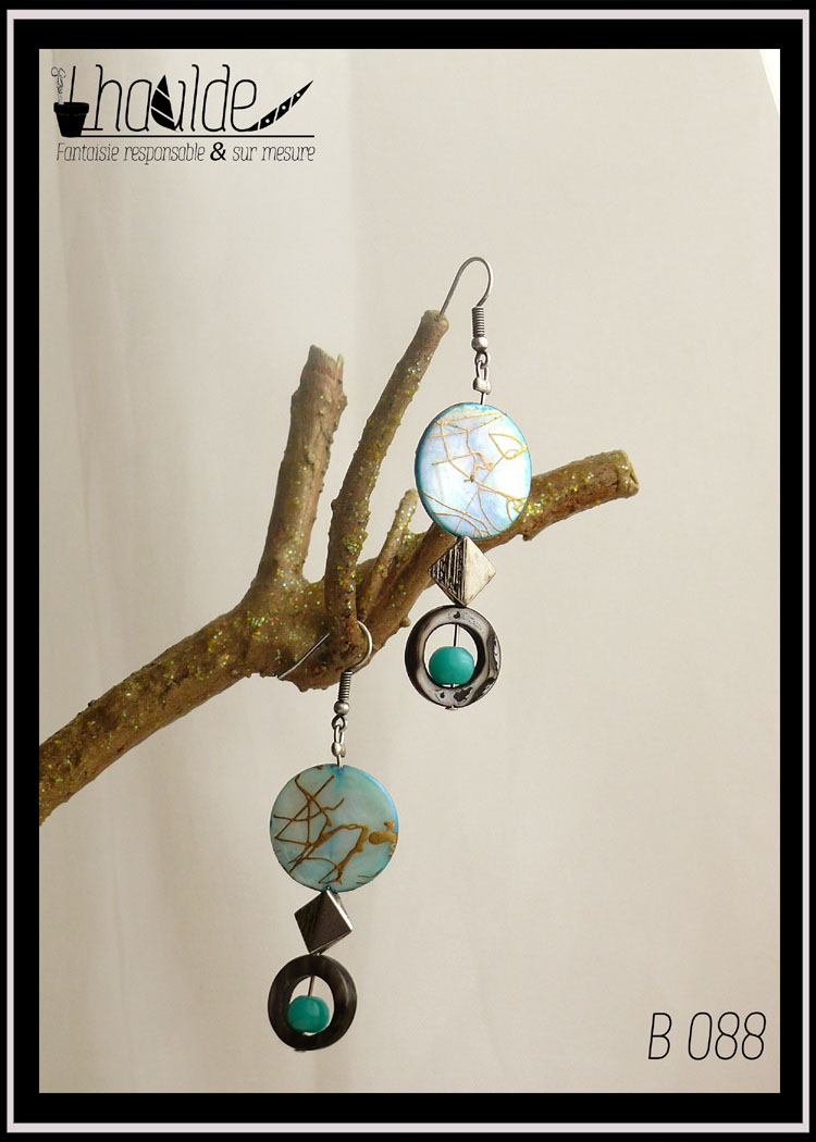 Paire de boucles d'oreilles. Crochet acier. Perles en nacre, verre et acier montées sur tige acier. Perle plate en nacre bleu marbré de doré, perle creuse circulaire en nacre gris avec au centre une perle ronde en verre opaque bleu,. Longueur 6,7 cm