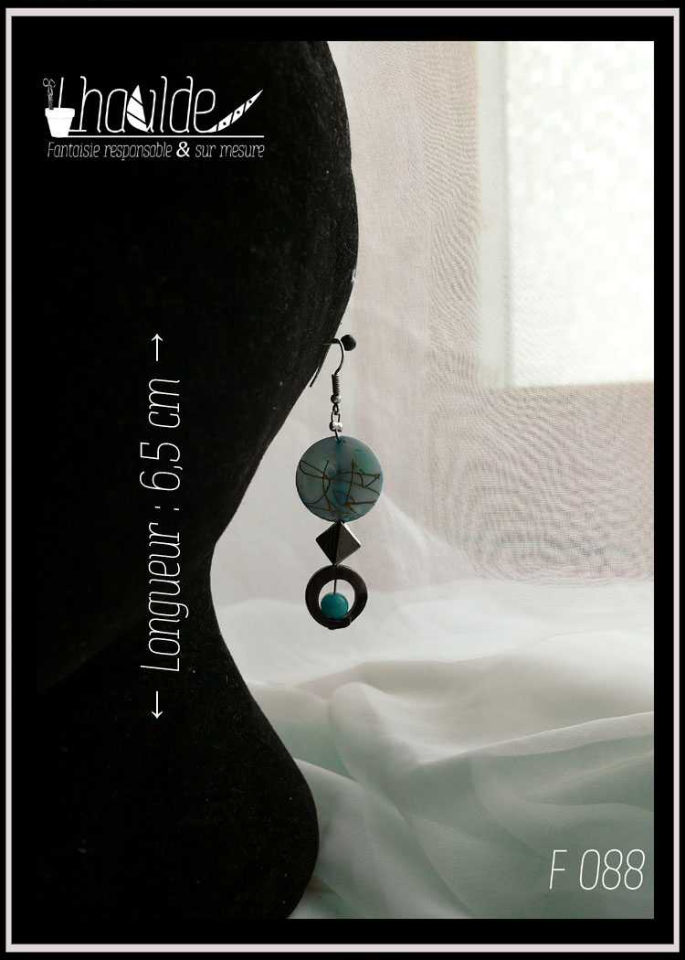 Paire de boucles d'oreilles. Crochet acier. Perles en nacre, verre et acier montées sur tige acier. Perle plate en nacre bleu marbré de doré, perle creuse circulaire en nacre gris avec au centre une perle ronde en verre opaque bleu,. Longueur 6,7 cm vues sur un mannequin tete