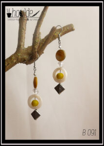 Paire de boucles d'oreilles. Crochet acier. Perles en nacre, verre et acier montées sur tige acier. Perle plate en nacre jaune, perle plate creuse circulaire en nacre blanc avec au centre une perle en verre opaque jaune et pour finir une perle carrée biseautée en acier. Longueur 6,5 cm