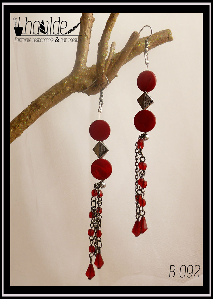 Paire de boucles d'oreille extra longue. Crochet acier. Perles plates en verre rouge imitation nacre, perle carrée biseautée en acier et chaine anneaux en acier avec perles en plastique rouge intercalées. Longueur 11,5 cm