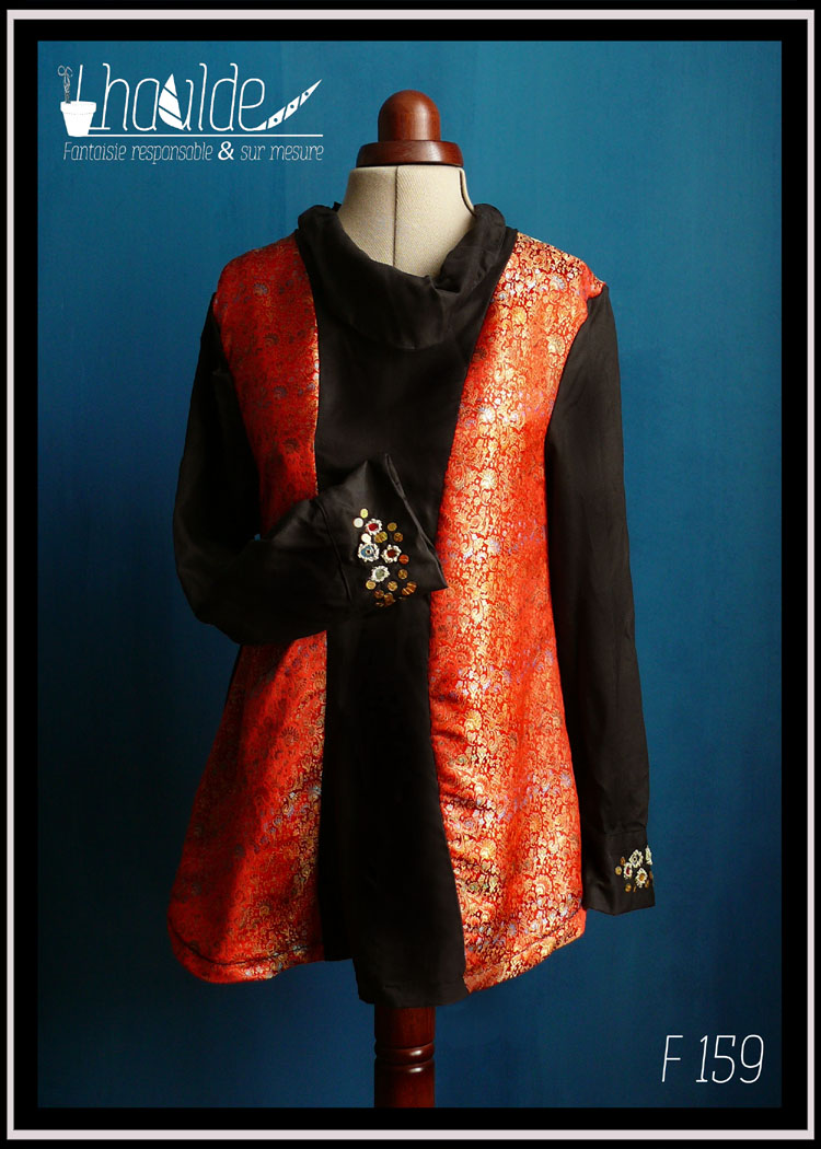 Tunique longue à manches longues. Centre, col, manches et dos en tencel noir. Manchettes brodées de perles et de miroirs. Côtés devant en soie synthétique rouge brocardée de motifs dorés Vue de face sur un mannequin de couture