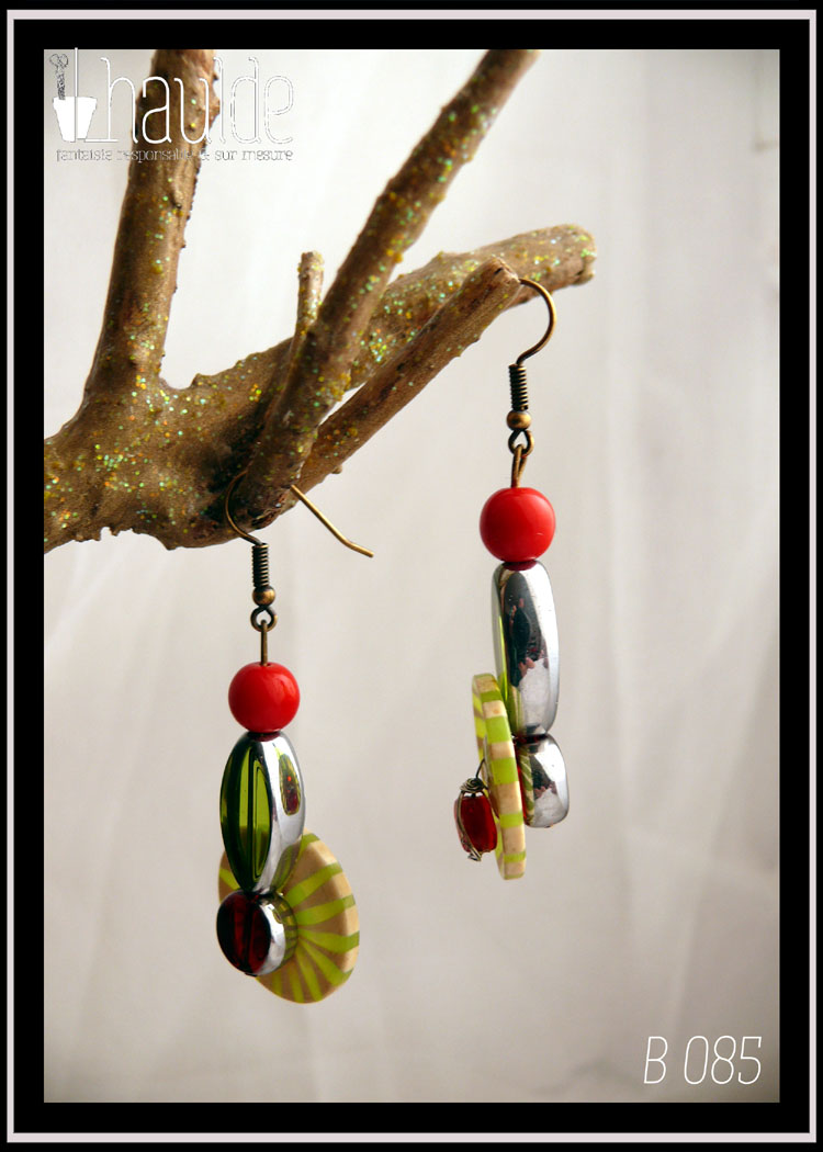 Paire de boucles d'oreilles, crochet acier. Bouton vintage en plastique rayé vert et vert pâle (les rayures partent du centre du bouton vers l'extérieur, comme des rayons) monté sur tige acier avec en son centre une perle en verre rouge avec une tranche en acier, au dos une perle en verre rouge biseauté et au-dessus une perle oblongue en forme de feuille en verre vert avec tranche acier et une perle en verre opaque rouge. Longueur 6,5 cm