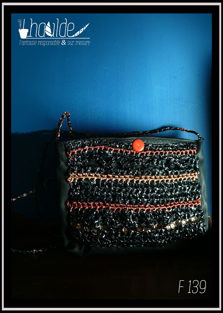 mini pochette en simili cuir noir doublé de coton imprimé motifs végétaux orange pâle sur fond vermillon. Devant couvert de VHS et fil de broderie crochetés et brodés de sequins dorés