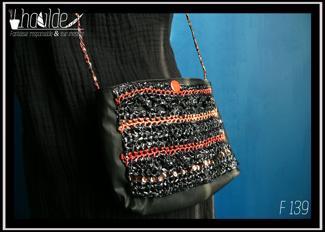 mini pochette en simili cuir noir doublé de coton imprimé motifs végétaux orange pâle sur fond vermillon. Devant couvert de VHS et fil de broderie crochetés