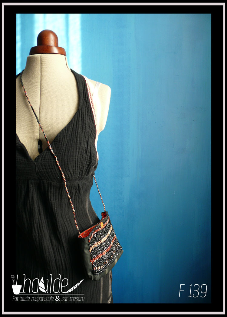 mini pochette en simili cuir noir doublé de coton imprimé motifs végétaux orange pâle sur fond vermillon. Devant couvert de VHS et fil de broderie crochetés Vu porté par un mannequin de couture