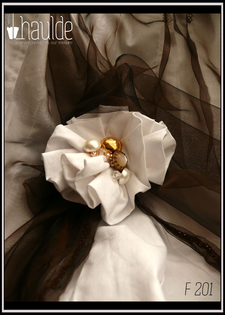 Jupe asymétrique plissée façon kilt en popeline blanche voilée d'organza marron à reflets cuivrés, l'organza est remonté sur le côté droit par une fleur en popeline blanche avec en son centre des boutons et des perles de rocailles dorées et nacrées. Vue de détail de la fleur de tissu