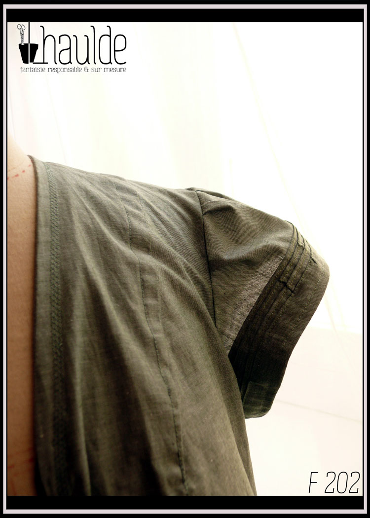 Combinaison manches très courtes et plissé, bande de tissu plissé en bas du ventre et poches plaquées plissées sur le devant des jambes. Zip central devant et taille soulignée par un élastique. Détail d'une manche