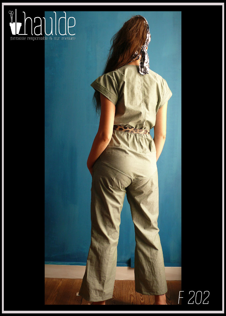 Combinaison manches très courtes et plissé, bande de tissu plissé en bas du ventre et poches plaquées plissées sur le devant des jambes. Zip central devant et taille soulignée par un élastique. Vue portée en pied de dos