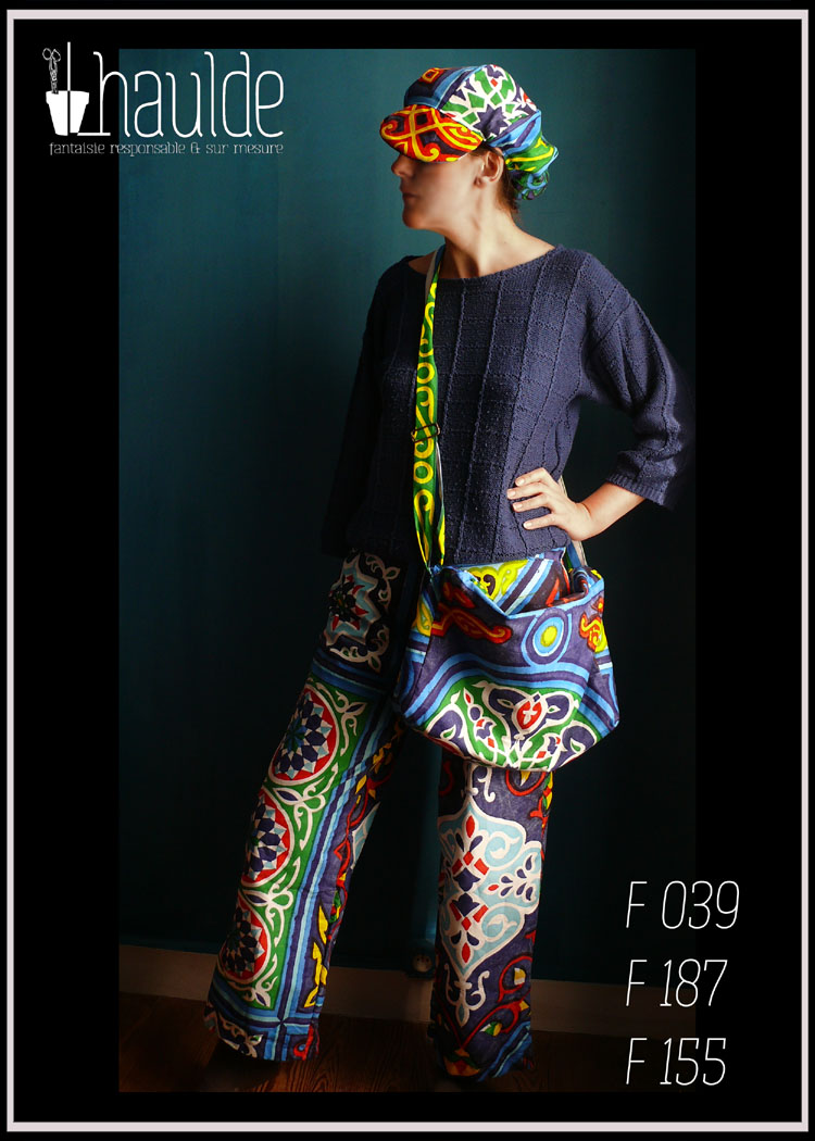 femme debout de profil portant un pantalon, une casquette et un sac assorti en toile bleue imprimé "carreaux égyptien" de grands motifs de carrelage aux couleurs vives, dominante bleue avec du rouge du jaune et du vert