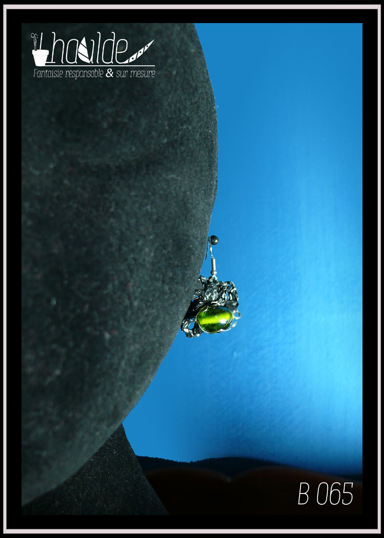 paire de boucles d'oreilles en VHS crochetée montée sur crochet d'acier. Vidéo crochetée de forme ovale avec en son centre une grosse perle en verre vert. Vue sur une tête de mannequin