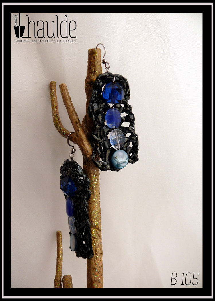 paire de boucles d'oreilles en bande vidéo crochetée montée sur crochet acier avec au centre, alignées à la verticale, quatre perles allant du bleu foncé (en haut) au bleu clair) en bas. Une perle en forme de dodécaèdre en plastique bleu foncé, deux perles ovales plates en verre transparent bleu roi et bleu clair et pour finir une perle plate circulaire en nacre bleu pâle