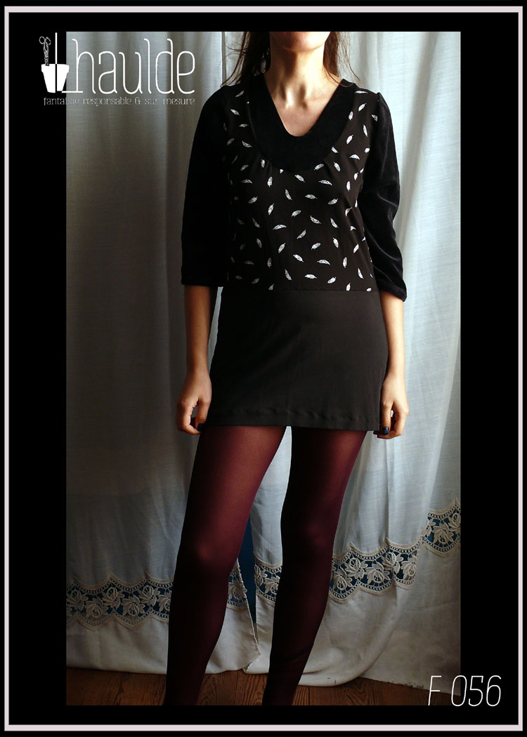 Robe courte à manches longues en jersey noir, jersey noir imprimé plumes blanches au centre en haut devant et dans le dos et velours noir autour de l'encolure en V plongeant Vue de face, portée par une grande femme d'1.78m debout, la jupe lui arrive en haut des cuisses