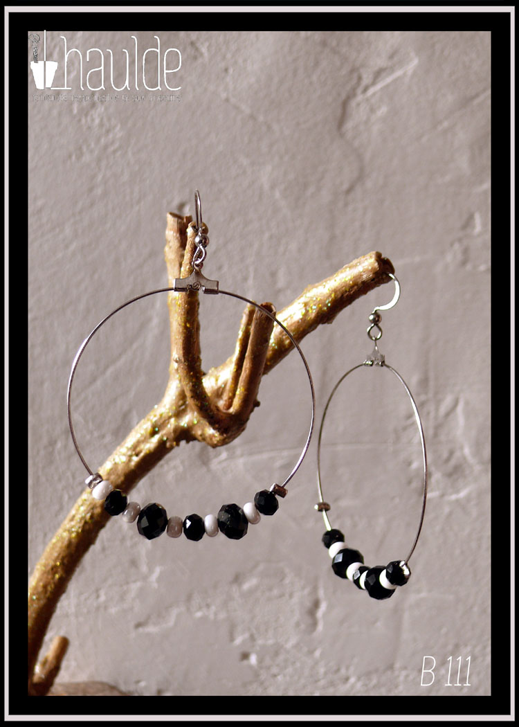 Paire de boucles d'oreilles montées sur une fine créole d'acier avec un crochet. Perles noires et blanches alternées, grosse rocaille pour le blanc, perles en verre biseauté pour le noir