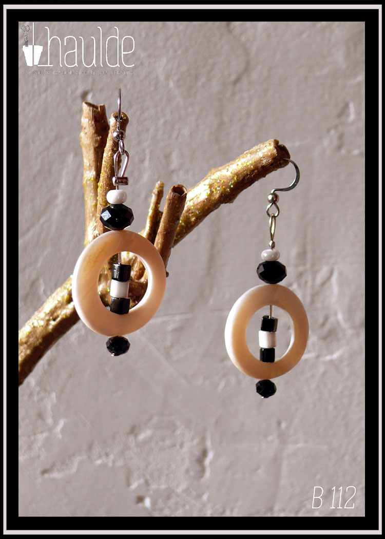 Paire de boucles d'oreilles montées sur tige et crochet d'acier. De haut en bas : une perle de rocaille blanche, une perle de verre biseauté noir, un cercle de nacre blanc avec au centre deux perles cubiques en verre, une noire, l'autre blanche et pour finir une perle en verre biseauté noir.