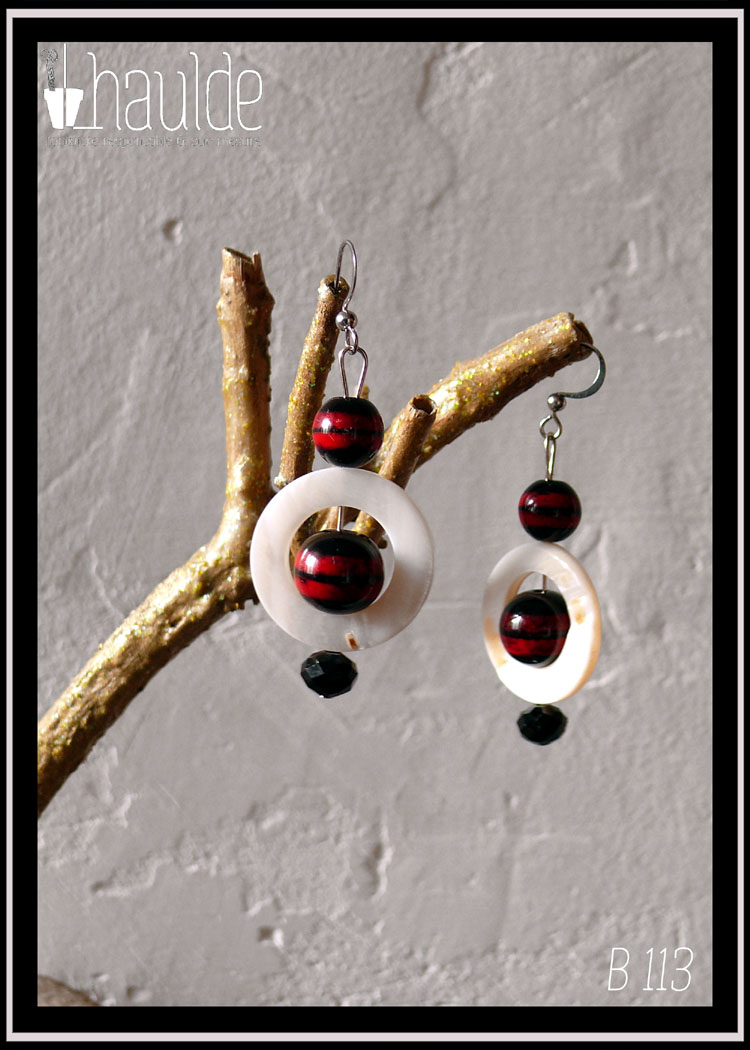 Paire de boucles d'oreilles montées sur tige et crochet d'acier. Avec de haut en bas : une perle ronde noire rayée de rouge, un cercle de nacre blanc avec à l'intérieur une perle noire rayée de rouge un peu plus grosse que la précédente et pour finir une pierre en verre noir biseauté