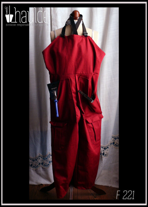 salopette rouge foncé posée sur un mannequin de couture avec des outils qui sortent des poches