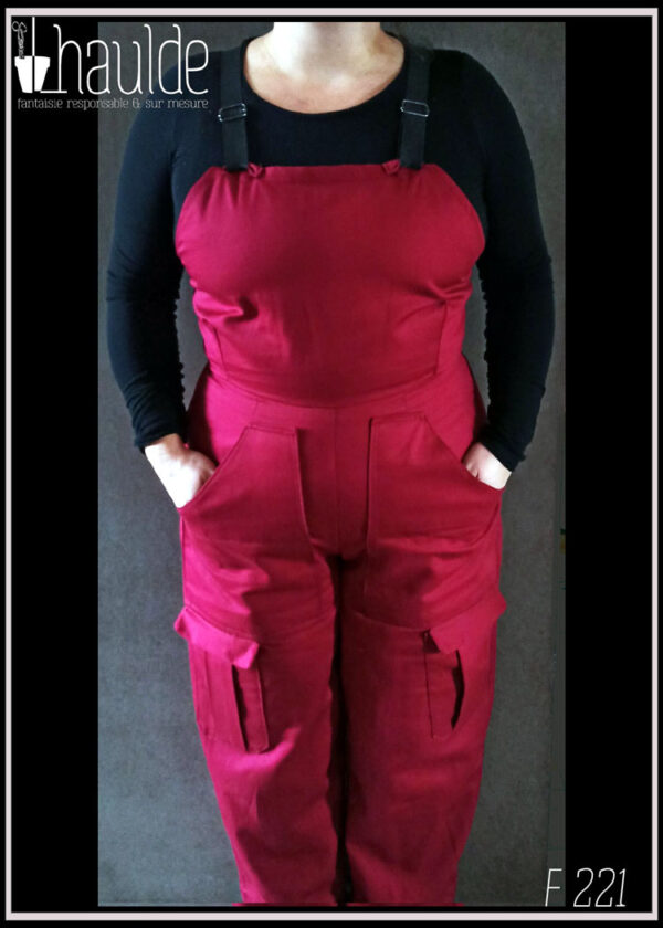 Salopette en toile rouge foncé, bretelles élastiques noires avec boucles de réglage, poches multiples hanches et cuisse, portée vue de face