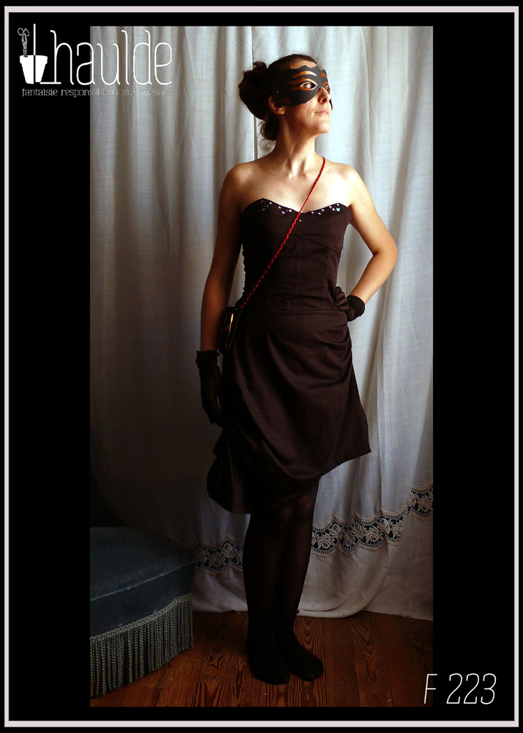 Robe bustier en satin de coton noir courte à jupe asymétrique plissée et haut à pans façon corset. Le haut du bustier est brodé de sequins et de perles de rocailles mauve, violettes, vertes et irisées Vue portée de face