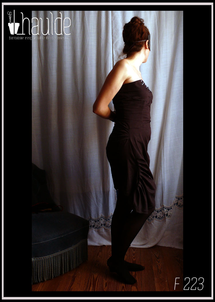 Robe bustier en satin de coton noir courte à jupe asymétrique plissée et haut à pans façon corset. Le haut du bustier est brodé de sequins et de perles de rocailles mauve, violettes, vertes et irisées Vue portée de profil droit