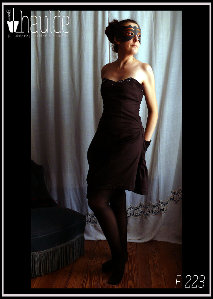 Robe bustier en satin de coton noir courte à jupe asymétrique plissée et haut à pans façon corset. Le haut du bustier est brodé de sequins et de perles de rocailles mauve, violettes, vertes et irisées Vue portée de trois quart gauche