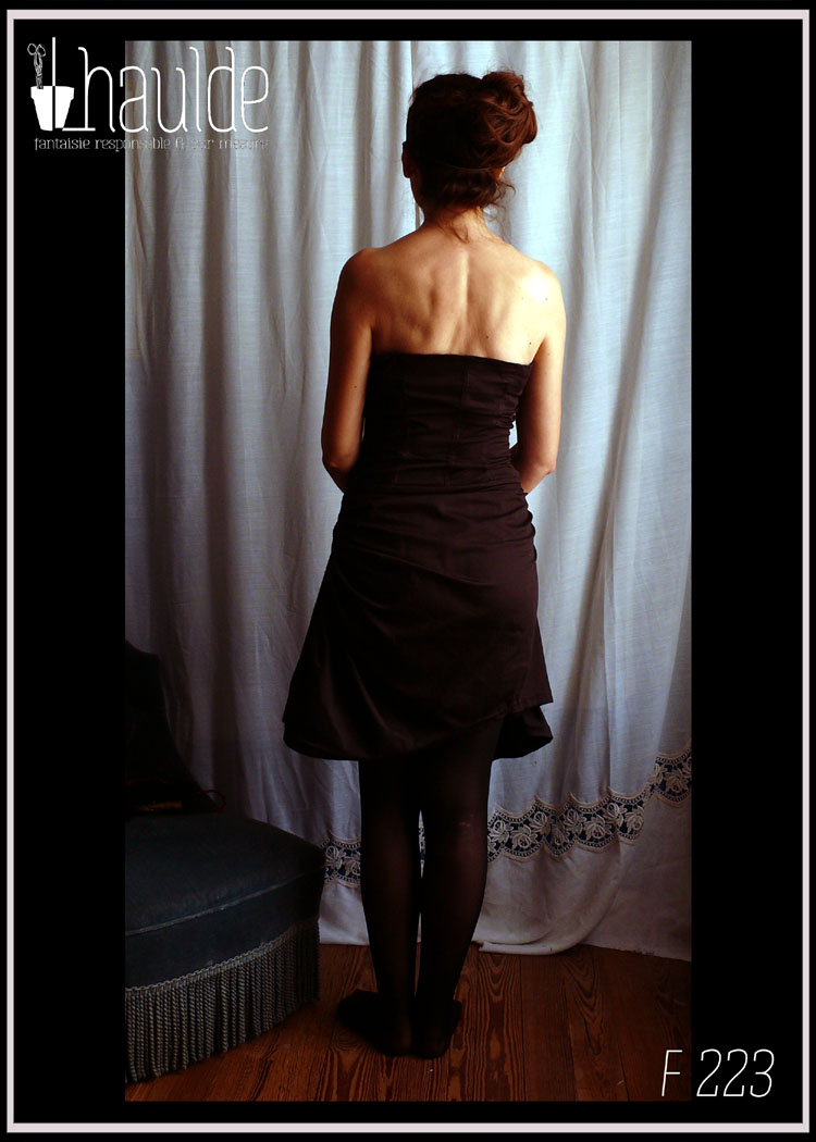 Robe bustier en satin de coton noir courte à jupe asymétrique plissée et haut à pans façon corset. Le haut du bustier est brodé de sequins et de perles de rocailles mauve, violettes, vertes et irisées Vue portée de dos