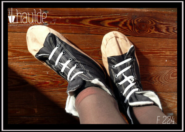 Paire de chaussons façon converse, bout et bande inférieure beige, haut du pied et semelle noirs. Lacets élastiques blancs