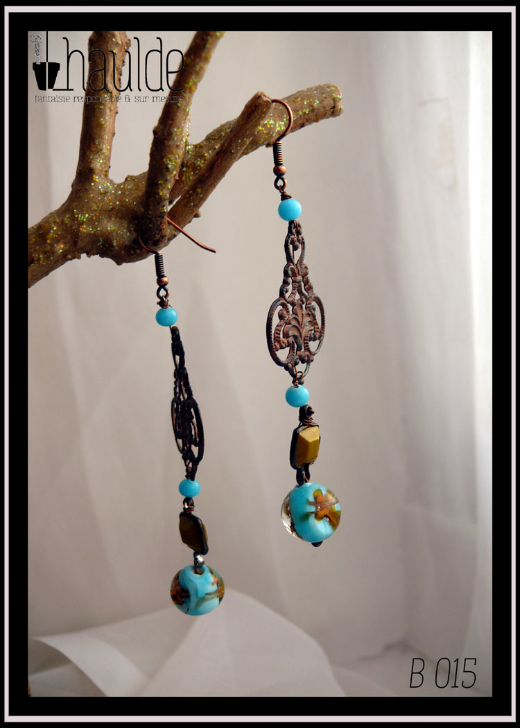 Boucles d'oreilles longues montées sur crochet d'acier, petite perle ronde couleur turquoise, estampe couleur bronze, petite perle ronde couleur turquoise, perle carrée vert-jaune enchassée dans de l'acier, perle bleue ronde à incrustation dorée