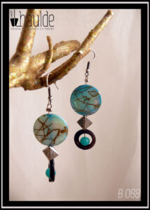 Paire de boucles d'oreilles. Crochet acier. Perles en nacre, verre et acier montées sur tige acier. Perle plate en nacre bleu marbré de doré, perle creuse circulaire en nacre gris avec au centre une perle ronde en verre opaque bleu,. Longueur 6,7 cm