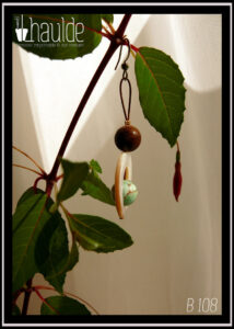 Paire de boucles d'oreilles montées sur crochet. Une perle de dickite marron, un cercle de nacre avec au centre une perle de dickite vert pâle et marron avec des effets de marbrure Vue suspendue à une branche de fuchsia