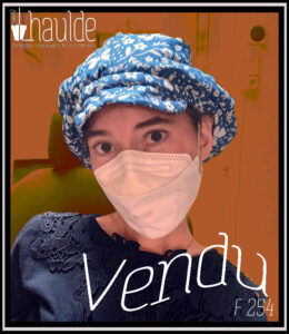 femme vue de face portant une casquette bleue imprimé papillons et fleurs blanches avec la mention "vendu"